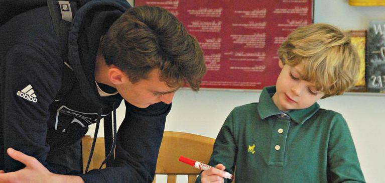 An Upper School Chase Collegiate student helps a Lower School student with his drawing.